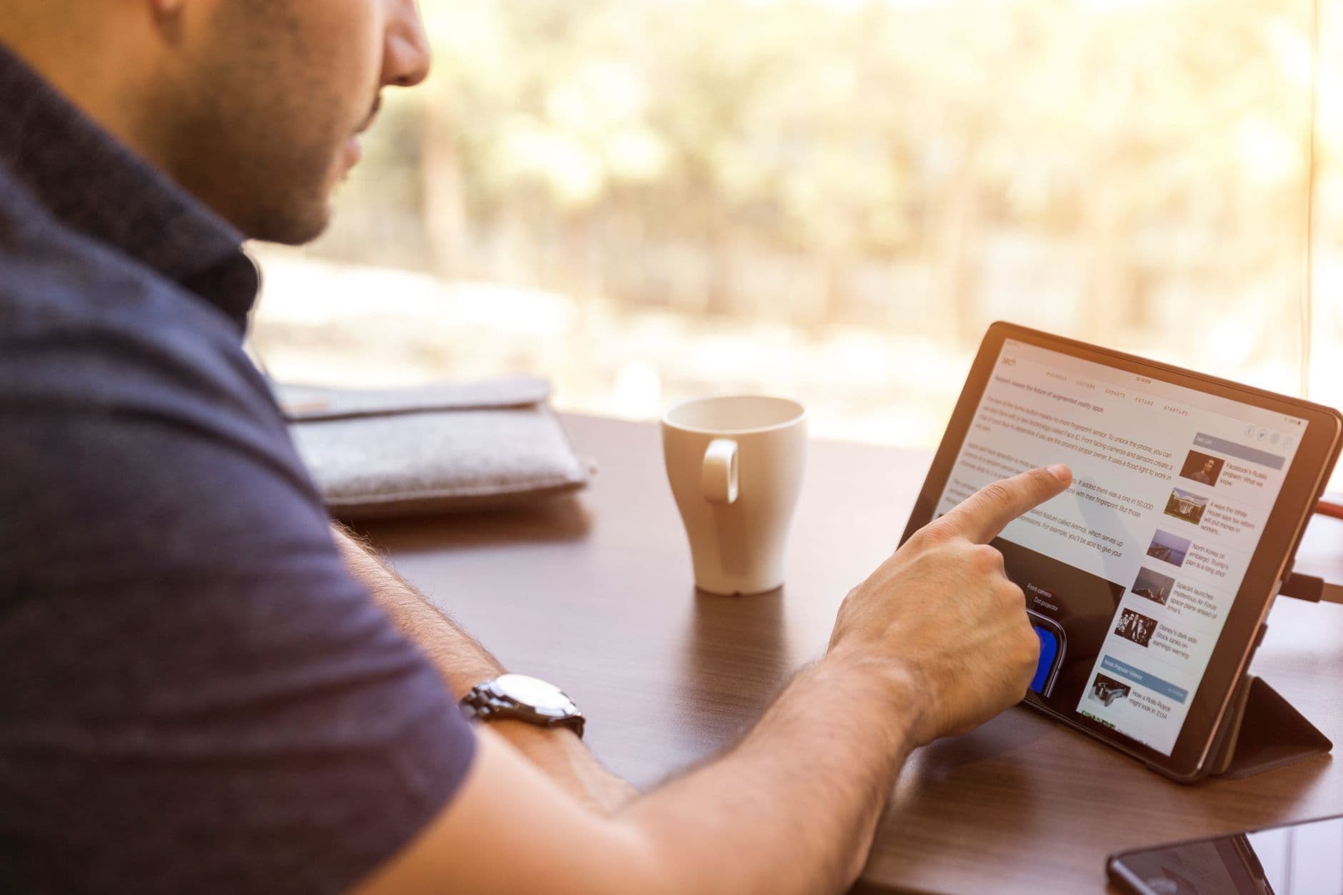 Adult man browsing a tablet with coffee indoors during the day.