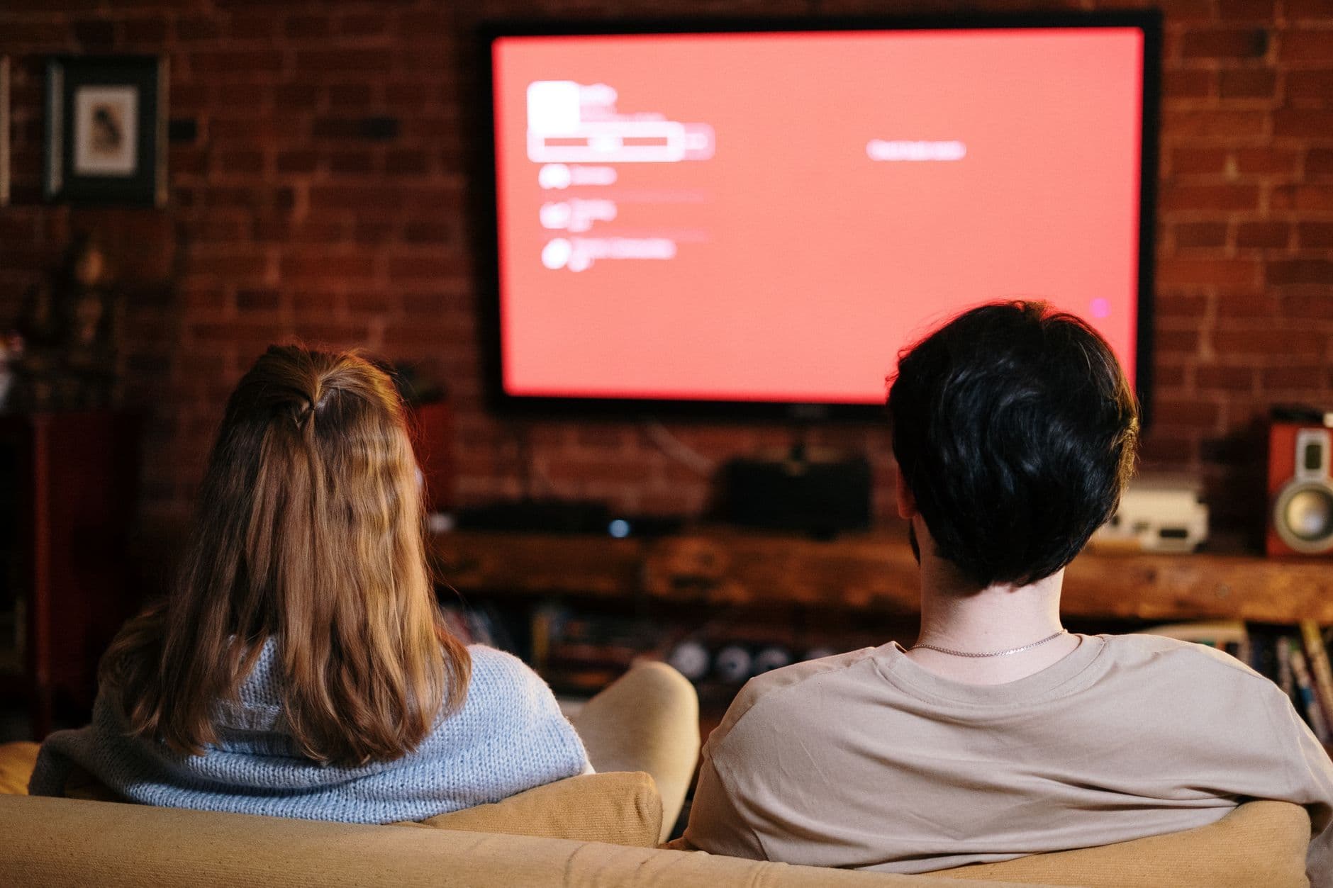 A couple watches TV together in a cozy brick-walled living room on a sofa.